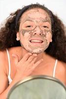 mooi vrouw Verwijderen klei gelaats masker van haar gezicht foto