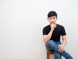 Aziatisch Mens zittend Aan stoel met zelfverzekerd gezicht op zoek Bij camera Aan wit achtergrond foto