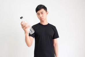 Aziatisch Mens zwart overhemd Holding plastic fles in hand- en kijken Bij camera verward gezicht Aan wit geïsoleerd achtergrond foto