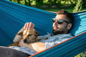 schattig weinig hond is gieren. resting van hond met zijn eigenaar in hangmat Aan zonnig zomer dag. foto