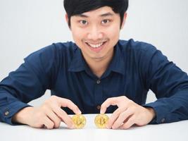 Aziatisch Mens zittend Bij de bureau glimlachen gezicht met gouden bitcoins in zijn hand- foto