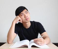 jong Mens zitten Bij de bureau verward met de boek in hand- Aan wit geïsoleerd foto