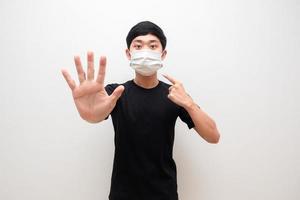 Aziatisch Mens tonen hand- hou op en punt Bij beschermen masker Bij zijn gezicht Aan wit achtergrond foto