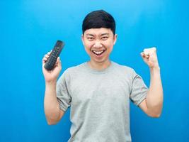 Aziatisch Mens Holding afgelegen controle televisie tonen vuist omhoog gelukkig emotie blauw achtergrond foto