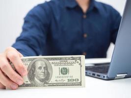 detailopname Mens hand- Holding geld dollar Aan de tafel met laptop Bijsnijden schot foto