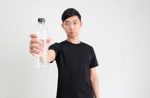 jong Aziatisch Mens zwart overhemd Holding plastic fles in hand- met zelfverzekerd gezicht Aan wit geïsoleerd achtergrond foto