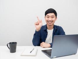 Mens glimlachen en punt vinger Bij kopiëren ruimte Bij werkplaats en laptop Aan de bureau foto