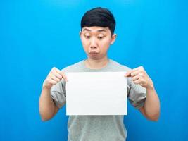 Aziatisch Mens gebaar twijfel op zoek Bij blanco vel in hand- blauw achtergrond foto
