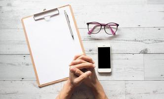 hand- met zilver pen Aan klembord en bril en smartphone Aan wit hout tafel natuur schaduw top visie foto