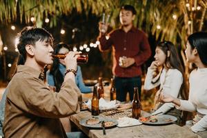 gelukkig vrienden juichen en drinken bier Bij een buitenshuis partij buitenshuis foto