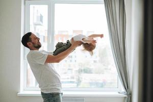 jong Mens vader hebben pret met baby meisje in de buurt venster Bij huis foto