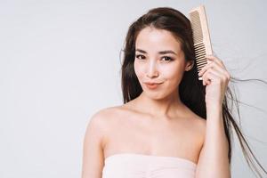 schoonheid portret van gelukkig glimlachen Aziatisch vrouw met donker lang haar- kammen houten kam Aan wit achtergrond geïsoleerd foto