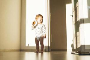 schattig baby meisje in leeg kinderen kamer met moeilijk licht Bij huis foto