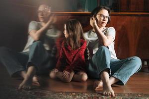 tween meisje en haar moeder zittend Aan de verdieping in leven kamer Bij de huis, kind op zoek Aan reflectie foto