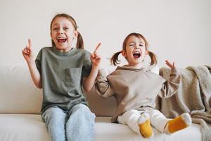 grappig gelukkig twee kinderen meisjes zussen hebben pret Aan bankstel Bij de huis foto