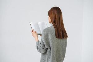 mooi jong vrouw met donker lang haar- in grijs gebreid trui lezing boek Aan de wit achtergrond foto