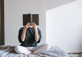 jong vrouw met donker lang haar- in gewoontjes kleren lezing boek Aan bed Bij de huis foto