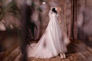 elegant en mooi bruiloft jurk. klassiek kant zijde bruiloft jurk hangende Aan hanger in hotel houten kamer. ochtend- voorbereiding bruiloft concept. foto