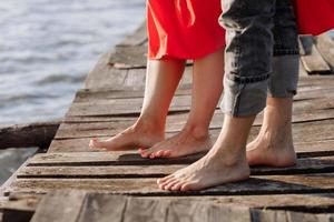 bijgesneden foto jonge geliefden getrouwd stel, man en vrouw, hand in hand op een houten brug in de buurt van meer. achteraanzicht van paar staande op de pier. onderste helft. plaats voor tekst en ontwerp. detailopname.