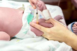 beeld van een verpleegster handen is gebruik makend van een injectiespuit geleidelijk vaccineren Aan ziek pasgeboren baby's been. foto