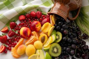 een gekleurde regenboog van bessen en fruit gemorst uit van de kruik. de concept van gezond aan het eten. top visie foto