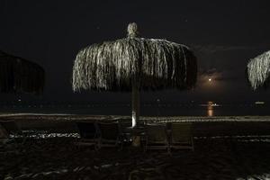 leeg dek stoelen en rieten parasols geregeld Aan zanderig strand Bij nacht foto