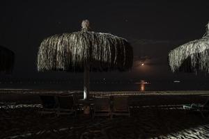 ligstoelen en rieten parasols geregeld Aan zanderig strand Bij nacht foto