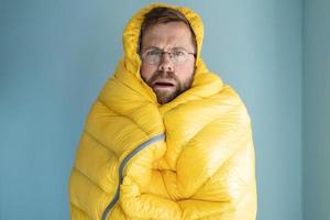 gealarmeerd Mens bevroor en verpakt zichzelf in een warm slapen tas, staand binnenshuis tegen de achtergrond van een muur. energie crisis concept. foto