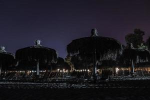 silhouet ligstoelen en paraplu's geregeld Aan strand onder lucht Bij nacht foto