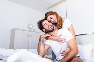 vrouw omarmen haar partner in bed, gelukkig paar in bed tonen emoties en liefde. mooi liefhebbend paar zoenen in bed. mooi jong paar aan het liegen samen Aan de bed. foto