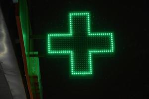 groen kruis apotheken Bij nacht in de stad. gloeiend met LED lampen, de groen kruis van de ziekenhuis. foto