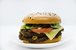 dubbele vlees hamburger met groenten Aan een wit achtergrond. heerlijk cheeseburger Aan een bord. vlees snel voedsel. een groot Hamburger met een dubbele kotelet. foto