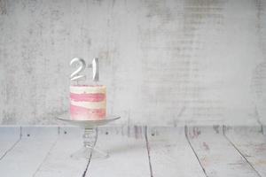 21e verjaardag taart roze en zilver taart met sommige hagelslag en 21e kaarslicht Aan een wit houten achtergrond. foto