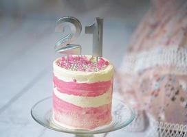 21e verjaardag taart roze en zilver taart met sommige hagelslag en 21e kaarslicht met een vrouw jurk in de achtergrond. foto