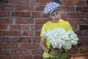 vrolijk gelukkig dorp kind met een boeket van bloemen. glimlachen weinig jongen met hortensia in de buurt de grunge steen muur. moeder dag, maart 8, Internationale vrouwen dag concept. foto