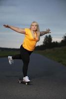 mollig middelbare leeftijd Europese vrouw, overgewicht, in een trainingspak, leert naar rijden een skateboard, gaat in voor sport. foto