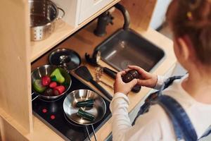 weinig meisje in gewoontjes kleren hebben pret door spelen met speelgoed Aan de keuken foto