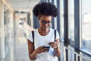jong Afrikaanse Amerikaans vrouw passagier in gewoontjes kleren is in luchthaven met kaartjes in handen foto