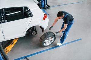 top visie. Mens in werk uniform wandelen met auto wiel binnenshuis. opvatting van auto- onderhoud foto