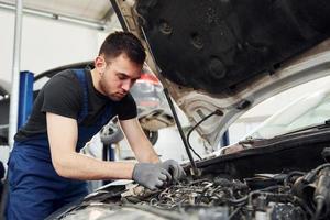 onder de kap. Mens in werk uniform reparaties wit auto- binnenshuis. opvatting van auto- onderhoud foto