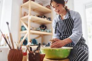 jong vrouw keramist werken door gebruik makend van pottenbakkerij wiel binnenshuis en maken handgemaakt klei Product foto