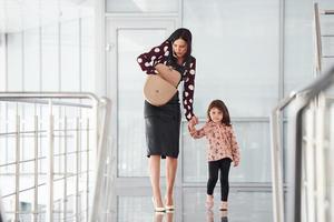 jong moeder met haar dochter wandelen samen binnenshuis in de kantoor of luchthaven. hebben vakantie foto