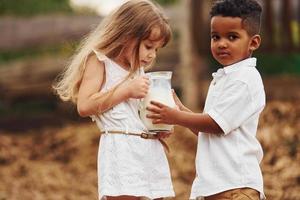 schattig weinig Afrikaanse Amerikaans jongen met Europese meisje is Aan de boerderij met melk foto