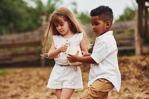 schattig weinig Afrikaanse Amerikaans jongen met Europese meisje is Aan de boerderij met melk foto