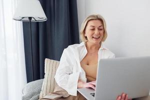 middelbare leeftijd vrouw in elegant kleren is Bij huis met laptop foto