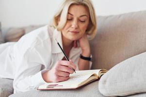 middelbare leeftijd vrouw in elegant kleren is Bij huis schrijven in kladblok foto