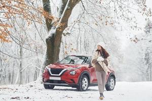 landelijk tafereel. mooi jong vrouw is buitenshuis in de buurt haar rood auto- Bij winter tijd foto