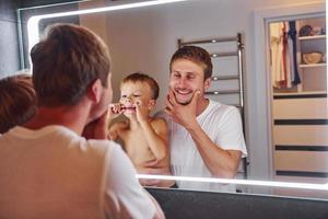 op zoek in de spiegel in badkamer. vader en zoon is binnenshuis Bij huis samen foto