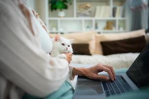 een jong vrouw werken Bij huis terwijl een wit Perzisch kat foto