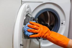 een Mens in geel handschoenen reinigt een vies, beschimmeld rubber zegel Aan een het wassen machine. gietvorm, aarde, kalkaanslag in de het wassen machine. periodiek onderhoud van huishouden huishoudelijke apparaten. foto